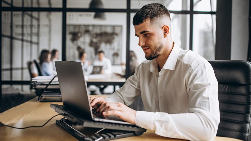 Na imagem está um homem empreendedor sentado e digitando no notebook em busca de conta PJ Pix gratuito.