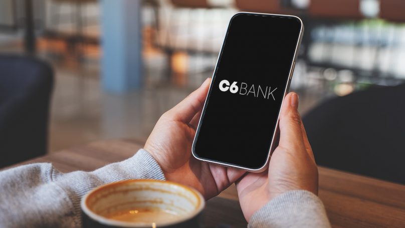 Na imagem está uma pessoa segurando um celular com a página do rendimento C6 Bank.