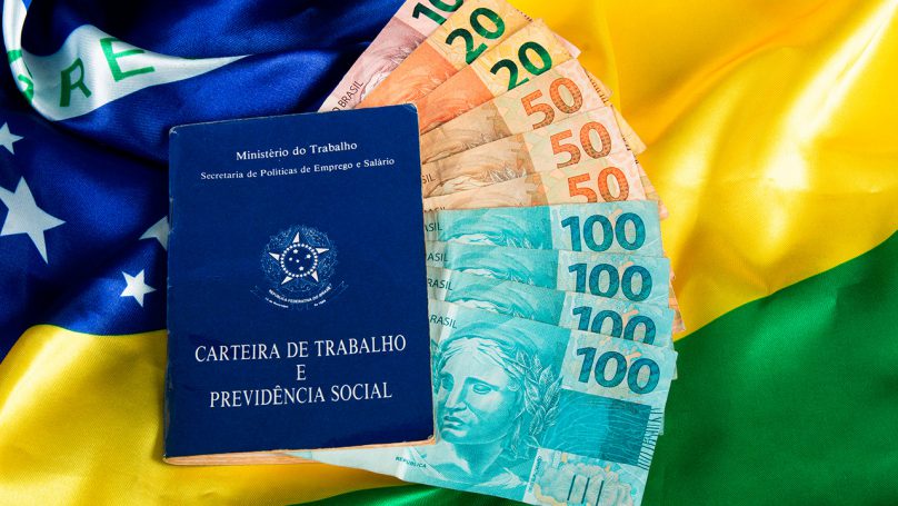 Foto de uma carteira de trabalho e algumas notas em dinheiro indicando o saque do FGTS.